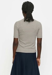 Bruine en witte gestreepte t-shirt met korte mouwen, aansluitend ontwerp en zachte textuur. Draag met een donkerblauwe rok, gezien van achteren.