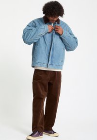 Denimjack met een bruine corduroy kraag, lichtblauwe kleur, grote zakken en drukknoopsluitingen. Combinatie met bruine corduroy broeken en donkere sneakers.