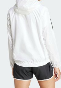 Valkoinen kevyt takki, jossa on huppu, kiristetty vyötärö ja mustat sivukoristeet. Yhdistetty mustiin urheilushortseihin, joissa valkoiset reunat.