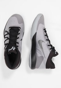 Szare i czarne buty sportowe z teksturowaną cholewką, wyściełanym wsparciem kostki oraz gumową podeszwą z charakterystycznym bieżnikiem. Srebrne logo Nike.