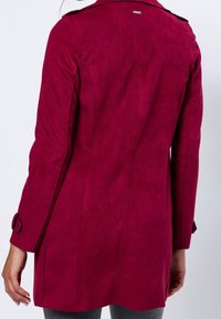 Magenta suède jas met een rugventilatie, schouderepauletten en met knopen sluitende manchetten, met een gladde textuur en een getailleerde pasvorm.