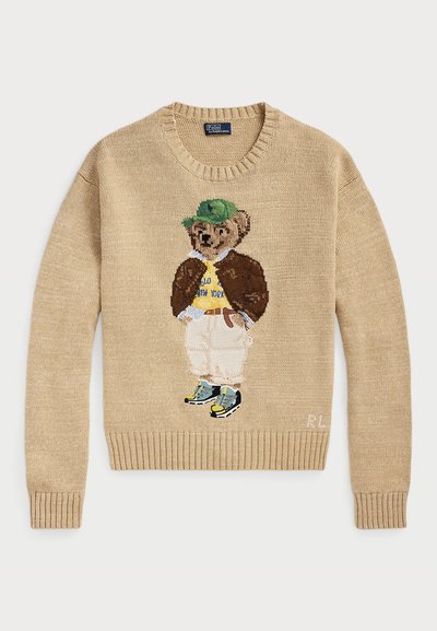 Beige gebreide trui met een geborduurd berenfiguur dat een groene hoed, een gele shirt, een bruine jas en lichte broek met sneakers draagt.