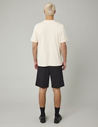 Chemise crème à manches courtes, shorts noirs, chaussettes noires et chaussures noires, vue de derrière ; design simple avec une coupe décontractée.