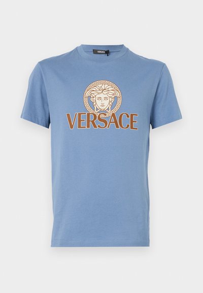 T-shirt de algodão azul com decote redondo, apresentando uma cabeça de Medusa dourada e o texto "VERSACE" em castanho. Mangas curtas e bainha reta.