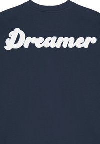 Jūros laivyno pavasarinis megztinis su iškiliais baltais siuvinėjimais, kuriuose užrašyta "Dreamer" (Sapnuotojas) ant nugaros. Klasikinis apvalios iškirptės dizainas ir minkšta tekstūra.