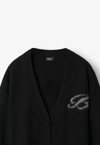 Cardigã preto feito de tecido texturizado, com decote em V, fecho de botão único e um logótipo cinza bordado no lado esquerdo.