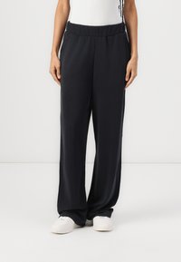 Mustad, vabalt istuvad püksid elastse vöökohtaga ja küljetaskutega, valmistatud siledast kangast. Kombineeritud valgete tossudega.