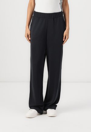Black, loose-fitting pants with an elastic waistband and side pockets, made from smooth fabric. Paired with white sneakers.