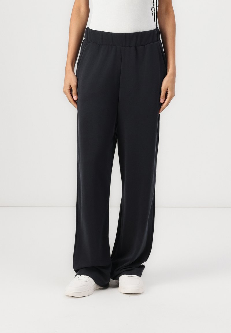 Mustad, vabalt istuvad püksid elastse vöökohtaga ja küljetaskutega, valmistatud siledast kangast. Kombineeritud valgete tossudega.