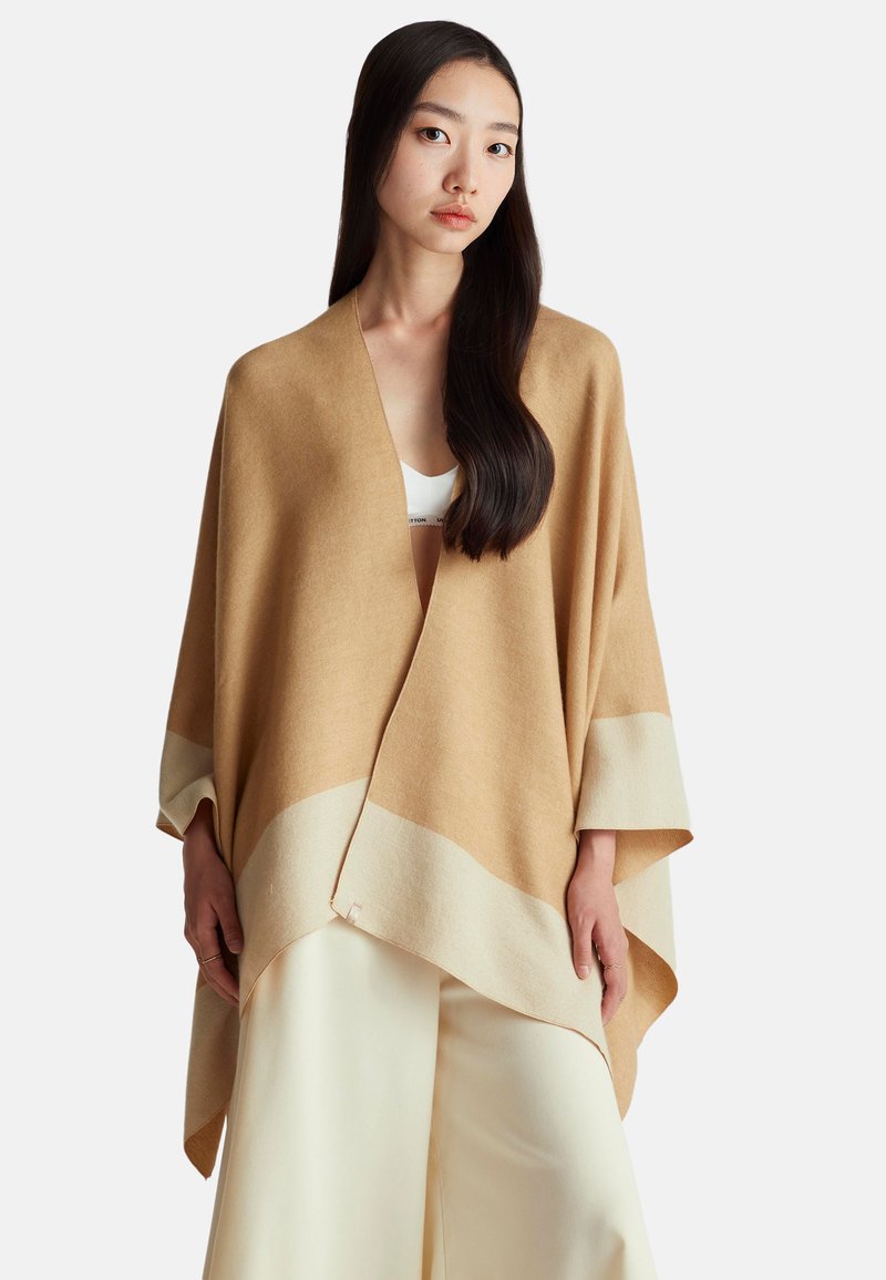 Béžový pončo z vlněné směsi s širokými rukávy a kontrastním krémovým lemem, s uvolněnou siluetou a hladkou texturou.