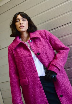 Fuksia villa segmendi mantel tekstureeritud viimistlusega, suur krae, esine nupud ja taskud, kantud valge särgi ja mustade pükstega.