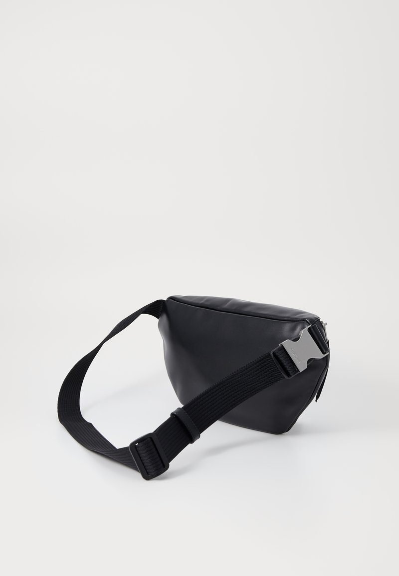 Sac synthétique noir de forme triangulaire, doté d'une bandoulière noire robuste et d'une boucle en argent. Texture lisse, fermeture éclaire sur le dessus.