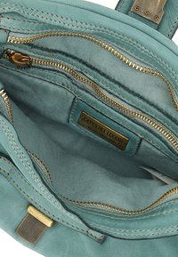Interno di una borsa in pelle color teal con più tasche con zip dorate, texture liscia e un'etichetta dorata con scritto "Caterina Lucchi."