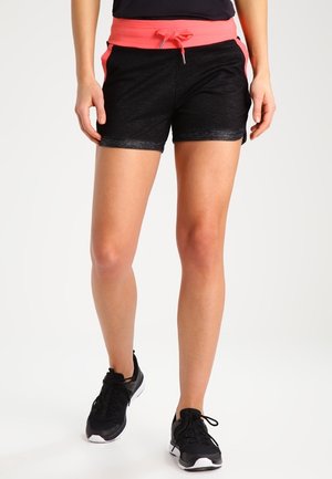 Vrouw draagt zwarte en roze sportshorts met trekkoord en zwarte hardloopschoenen, staand op een witte achtergrond.