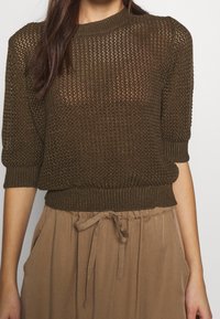 Bruin gebreid sweater met een gestructureerde open structuur, korte mouwen en een aansluitende geribbelde zoom, gecombineerd met losse tanbroek met een trekkoord.