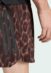 Ruskeat leopardikuvioiset shortsit mustilla raidoilla, joissa on joustava vyötärönauha ja sivuhalkio liikkuvuuden parantamiseksi, valmistettu synteettisestä kuidusta.