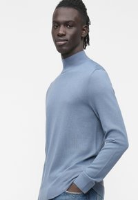 Svetlo modra pulover z visokim ovratnikom iz mehke tkanine. Ponaša se z rebrastim ovratnikom, dolgimi rokavi in sproščenim krojem s stranskimi razporki na spodnjem robu.