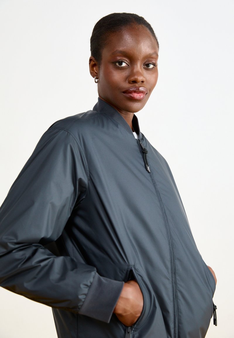 Ciemnoszara kurtka bombowiec z wysokim kołnierzem, zamkiem z przodu i kieszeniami po bokach. Wykonana z lekkiego materiału o gładkiej fakturze.