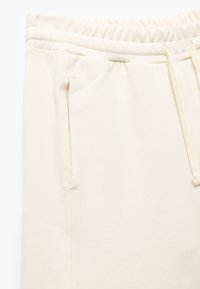 Beige joggers gemaakt van zachte stof, met een trekkoord in de taille, zijzakken en een gladde textuur.
