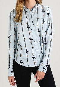 Ljusblå långärmad skjorta med ett vertikalt svart och guldmönster. Har en kraglös design och knäppning fram. Mjuk tygkvalitet.