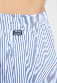 Blue and white striped boxers with an elastic waistband, featuring a Jockey label on the front. Made of lightweight cotton fabric.