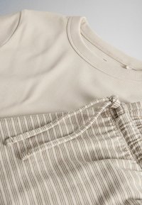 T-shirt crème à manches longues côtelé associé à un pantalon crème à cordon avec de fines rayures verticales marron, posé à plat sur un fond neutre.