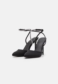 Svarta satinhöga klackar med spetsiga tår, smala ankelband dekorerade med strass och slanka stilettklackar. Minimalistisk design.