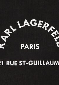Toile noire avec un texte blanc audacieux qui lit "KARL LAGERFELD PARIS 21 RUE ST-GUILLAUME" dans une disposition courbée. Le texte est clair et centré.