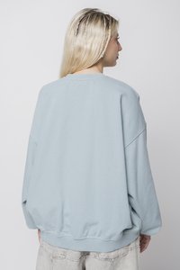 Hellblaues, übergroßes Sweatshirt aus weichem Material mit überschnittenen Schultern, geripptem Saum und Bündchen. Glatte Textur mit minimaler Gestaltung.