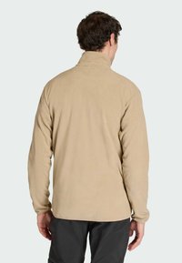 Beige fleece jack met een hoge kraag, lange mouwen en een gladde textuur. Heeft een rechte snit en geen zichtbare patronen of hardware.