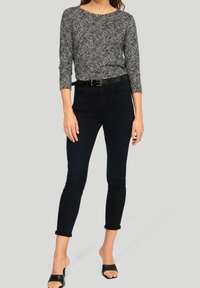 Schwarz-weißer gemusterter Langarm-Top mit Rundhalsausschnitt, kombiniert mit eng anliegenden dunklen Jeans und schwarzen sandalen mit offenen Zehen. Die strukturierte Stoffoberfläche ist sichtbar.
