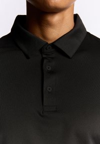 Sort polo-shirt med krave, tre-knaps placket og glat tekstur. Ingen synlige logoer eller mønstre.