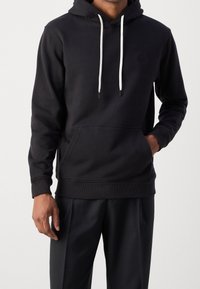 Sudadera negra hecha de un tejido suave, con un bolsillo canguro, cordones con acentos blancos y puños y dobladillo acanalados.