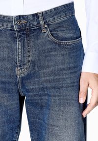 Dunkelblaue Jeans aus Denim mit einem klassischen Fünf-Taschen-Design, gerader Passform, Metallknopfverschluss und dezentem Verblassen des Stoffes.