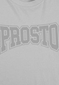 Jasnoszara koszulka z wyraźnym, pogrubionym logo "PROSTO" w ciemniejszym odcieniu szarości. Materiał ma gładkie, teksturowane wykończenie i okrągły dekolt.