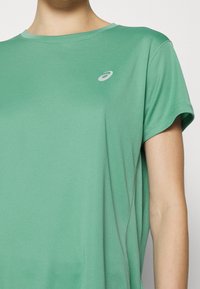 Camiseta atlética verde hecha de un tejido ligero y suave. Presenta un cuello redondo, mangas cortas y un pequeño logo en plata en el pecho.