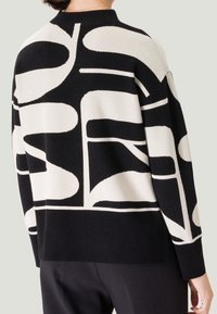 Sweter z dzianiny z odważnym czarno-białym abstrakcyjnym wzorem, wysokim dekoltem, prążkowanym wykończeniem oraz luźnym krojem. Miękka tekstura i nowoczesny design.