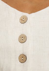 Top en lin beige clair avec un décolleté en V, présentant trois boutons ronds texturés d'apparence naturelle sur le devant.