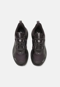 Black athletic shoes with mesh upper, padded collar, and rubber sole. Features elastic laces and logo accents on the tongue and sides.