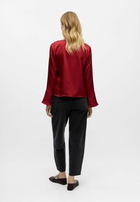 Röd satin-top med en avslappnad passform, långa klockärmar och rundad nederkant. Bärs med högmidjade svarta jeans och platta skor.