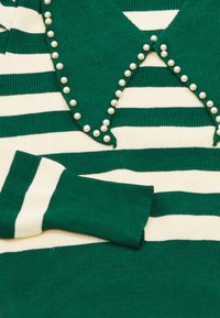 Maglione a righe verdi e crema con una texture a coste, dotato di un colletto decorato con piccole perle bianche lungo i bordi.