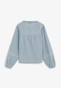 Camisa de mezclilla azul claro con canesú redondo, detalles fruncidos y mangas largas abullonadas. Presenta costuras blancas a lo largo del canesú y los puños.