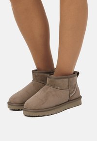 Botines cortos de ante marrón con punta redondeada y puño doblado, que presentan costuras texturizadas y suela de goma crepé.