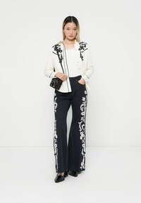 White button-up shirt with black floral embroidery, paired with navy pants featuring white floral patterns, and black shoes.