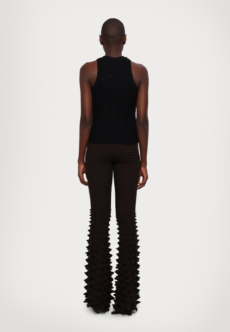 Schwarzes, geripptes, ärmelloses Oberteil kombiniert mit braunen, ausladenden Hosen mit einem strukturierten, gefransten Saum, der eine einzigartige Silhouette erzeugt.