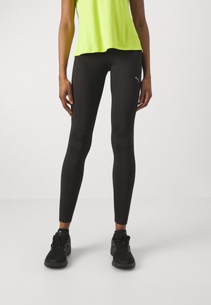 Leggings negros de tela elástica con una textura suave, combinados con una camiseta sin mangas de color verde brillante y zapatillas deportivas negras.