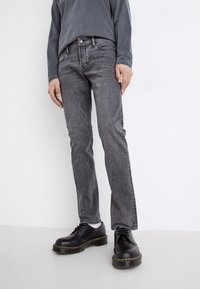 Grå denimjeans med rett passform, som har fem lommer og subtil søm. Kombinert med sorte snøresko og en mørk topp.