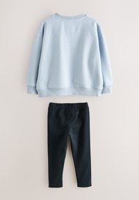 Šviesiai mėlynas džemperis su pūstais rankogaliais ir apačia, derinamas su juodais tampriais su elastinga juosmens juosta. Abu audiniai turi lygų paviršių.