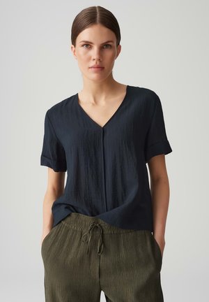 Top blu scuro a maniche corte con scollatura a V, realizzato in tessuto testurizzato. Abbinato a pantaloni plissettati di un verde chiaro con vita elasticizzata.