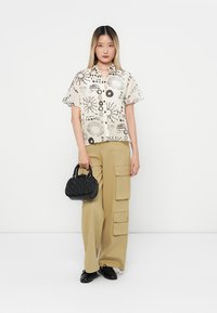 Korte ermers skjorte med abstrakt sort trykk på off-white stoff, kombinert med beige cargo-bukser og en liten svart håndveske.